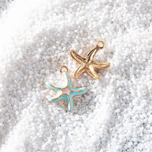 Golden and blue starfish alloy pendants for DIY jewelry making on white sand background