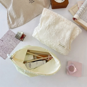 Close-up of lace embroidered makeup bags in cream and green with 3D flower patterns