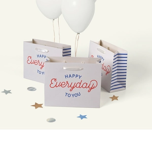 Detail of gray gift paper bag with colorful typography and premium white silk ribbon handles
