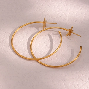Detail of gold star stud earrings with large circular hoop dangles on pink background