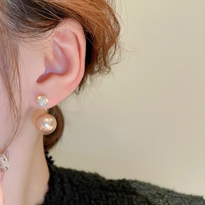 Close-up of elegant gold-plated earring with zircon and champagne pearl on ear