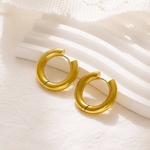 Close-up of thick gold-plated chunky hoop earrings on a minimalist white stone pedestal