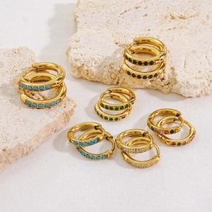 Elegant gold huggie earrings with colorful zirconia stones on minimalist stone display