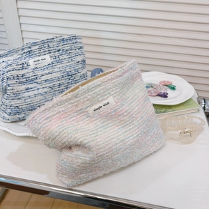 Detail of tweed makeup bags with simple wish labels on a cozy white desk setup