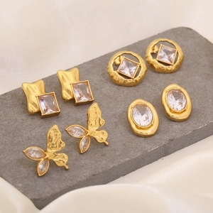Detailed view of four golden geometric and butterfly earrings on a textured stone