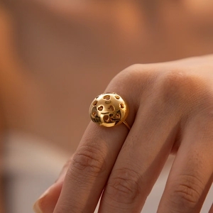 Close-up of a luxury gold hollow heart ball ring with polished metallic texture on finger