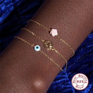 Three 925 sterling silver gold bracelets with rose, crystal, and evil eye charms on blue velvet