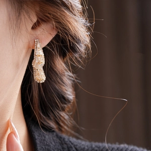 Close-up of elegant gold teardrop earrings with pavé zircons worn on ear