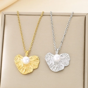 Gold and silver pleated leaf necklaces with pearl pendants in a beige jewelry box