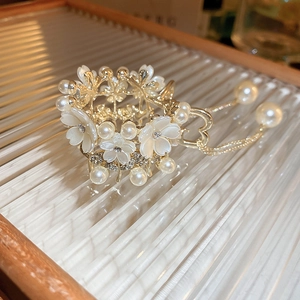 Detail view of flower hair claw with white petals, pearls, and heart tassel on glass