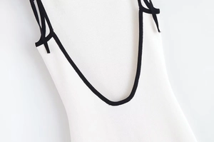Détail de robe en maille blanche avec bretelles noires et décolleté en V profond
