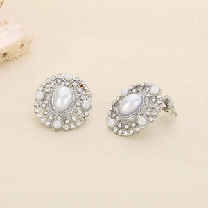 Macro detail of silver geometric stud earrings featuring central pearls and rhinestone halo