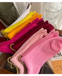 Gros plan de chaussettes en coton colorées rose, jaune et orange sur un support métal