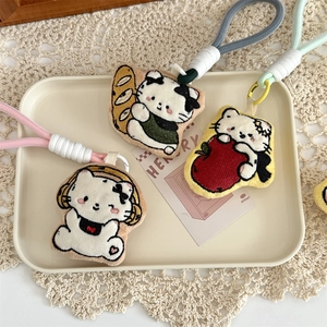Close-up of embroidered cat charms with woven lanyards on a cream-colored tray