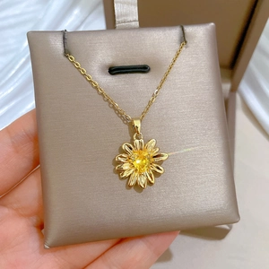 Macro shot of gold floral pendant necklace with yellow gem held in a jewelry box