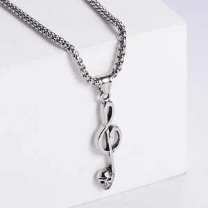 Macro side view of silver stainless steel skull music note pendant on a white geometric stand