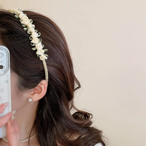 Detailed close-up of cream fabric roses and green leaves on a gold headband