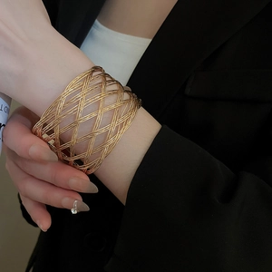 Detailed view of a wide gold woven lattice cuff bracelet worn over a black blazer sleeve