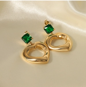 Detailed shot of gold heart earrings with green square gemstones on silk fabric
