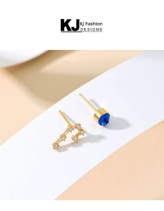 Asymmetric gold stud earrings featuring a blue center stone and celestial star patterns