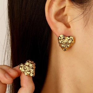 Detailed close-up of gold heart stud earrings featuring unique lava texture on ear
