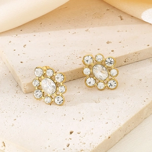 Detail of gold floral stud earrings with white zircons on a soft silk background