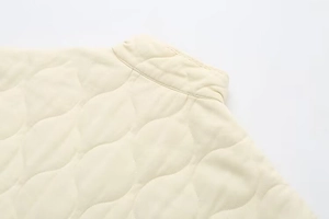 Detailed view of wave quilted pattern and stand collar on off-white padded jacket