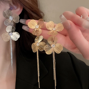 Détail de boucles d'oreilles fleurs à pompons avec texture métal brossé et strass