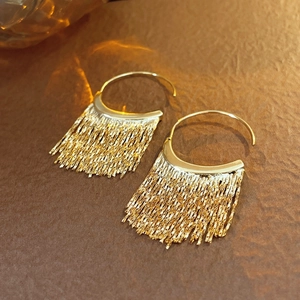 Détail de boucles d'oreilles dorées à pampilles avec base en C sur fond texturé