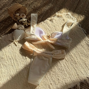 Detail of cream bikini top with golden starfish charm and bow on a beach mat