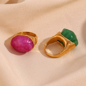 Detailed shot of two gold rings with pink and green irregular stones on silk fabric
