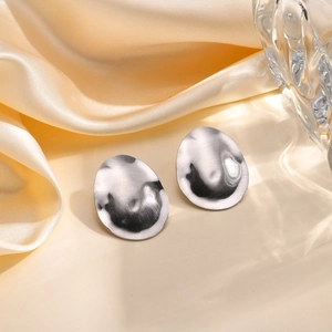Detail of silver brushed oval metal earrings on cream satin fabric with glass décor