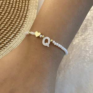 Close-up of white beaded bracelet featuring a gold heart and letter Q shell pendant
