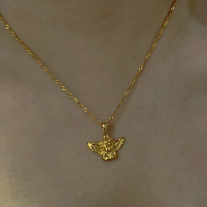 Gros plan d'un collier pendentif ange doré porté au cou avec une chaîne fine élégante