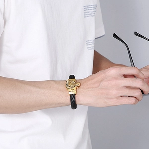 Detail of men's black braided leather bracelet featuring a gold carved wolf head clasp