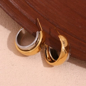 Macro detail of two-tone gold and silver C-shaped chunky hoop earrings on wood