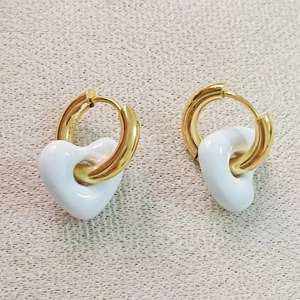 Gros plan de boucles d'oreilles créoles dorées avec pendentifs cœur en émail blanc