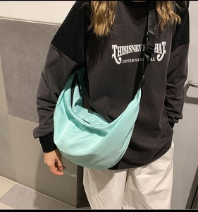Adjustable nylon crossbody crescent bag in light blue shown worn by a casual model