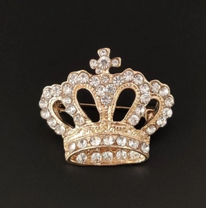 Close-up of golden crown brooch with sparkling white rhinestones on black background