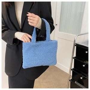 Close-up of a blue teddy plush tote bag held by a model wearing a black blazer