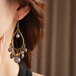Macro view of vintage bronze teardrop earrings with gray patterned beads on a model