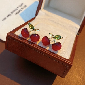 Macro shot of resin cherry earrings with green zircon leaves on a leather jewelry box