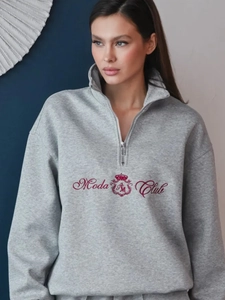 Close-up of grey half-zip sweatshirt featuring red Moda Club embroidery and crest detail