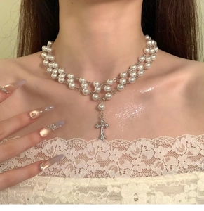 Detail of layered pearl necklace featuring a sparkling zircon cross pendant on a model