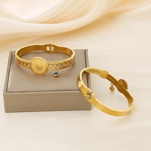 Detail of gold coin bangle with Greek pattern and blue evil eye charm on silk background