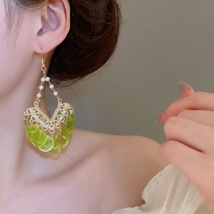 Detail of gold hollow earrings with white pearls and translucent green round shell charms