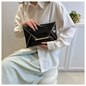Detail of black envelope clutch featuring glossy crocodile texture and gold metal clasp