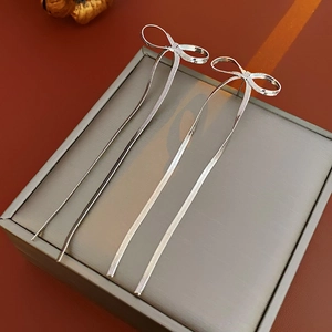 Détail de boucles d'oreilles nœud argenté avec pompons sur un coffret à bijoux
