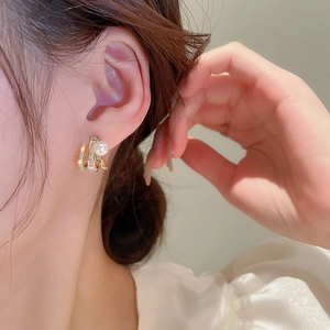 Close-up of elegant gold claw earrings with white pearl and sparkling zircon on model