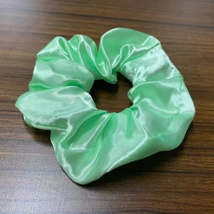 Detailed close-up of light green satin LED hair scrunchie on dark wooden background